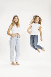 Selbstbewusstes Teenager-Mädchen mit springender Schwester vor weißem Hintergrund - SDAHF01197