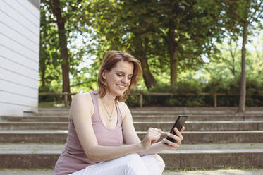 Happy woman text messaging on smart phone in park - BFRF02415