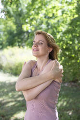 Smiling woman hugging self in park - BFRF02417