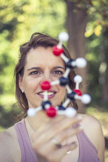 Lächelnde Frau, die ein Molekülmodell im Park untersucht - BFRF02423