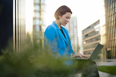 Geschäftsfrau arbeitet an einem Laptop und sitzt bei Pflanzen - MOEF04275