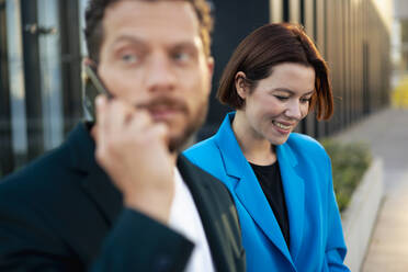 Young businesswoman looking down with colleague talking on smart phone - MOEF04288