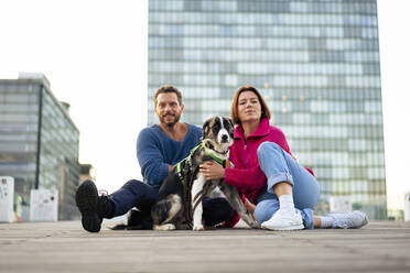 Couple sitting with pet dog in front of building - MOEF04291