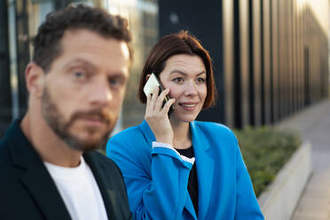 Contemplative businesswoman talking on smart phone by colleague - MOEF04292