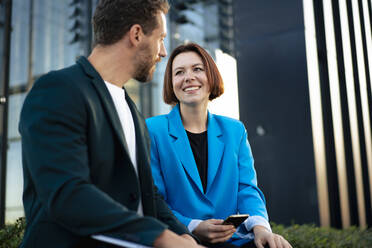 Happy business colleagues talking to each other in front of office building - MOEF04294