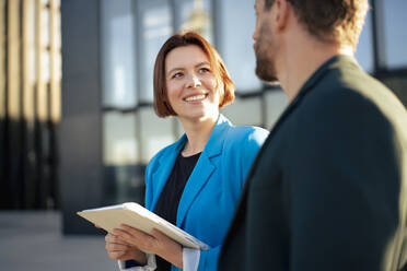 Lächelnde Geschäftsfrau mit Tablet-PC und Blick auf einen Kollegen an einem sonnigen Tag - MOEF04304