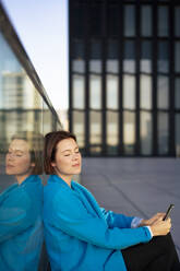 Businesswoman with eyes closed leaning on glass railing - MOEF04308