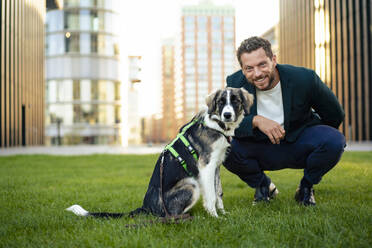 Smiling businessman with pet dog crouching on grass - MOEF04319