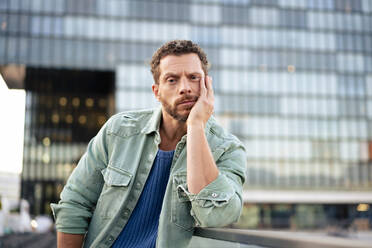 Man wearing denim shirt leaning on elbow at railing - MOEF04337