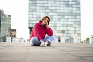 Junge Frau sitzt im Schneidersitz auf der Straße vor einem Gebäude - MOEF04341