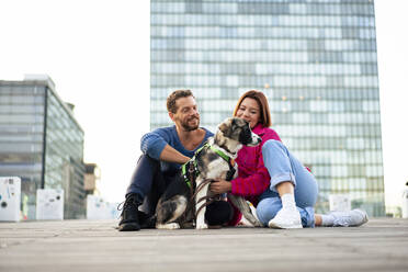 Happy couple spending leisure time with dog sitting on road in front of building - MOEF04342