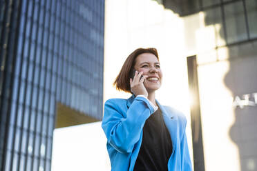 Happy businesswoman wearing blazer talking on smart phone - MOEF04352