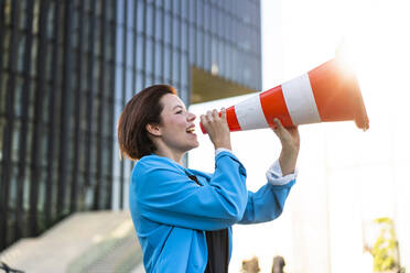 Businesswoman making announcement holding traffic cone - MOEF04360