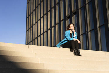 Geschäftsfrau sitzt auf einer Treppe in der Nähe eines Gebäudes - MOEF04362