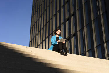 Junge Geschäftsfrau mit Tablet-PC auf einer Treppe sitzend - MOEF04363