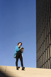 Geschäftsfrau mit Tablet-PC auf einer Treppe vor blauem Himmel stehend - MOEF04366
