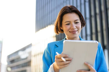 Lächelnde Geschäftsfrau mit Blick auf einen Tablet-PC - MOEF04374