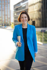 Lächelnde Geschäftsfrau in blauem Blazer beim Spaziergang mit Tablet-PC - MOEF04378