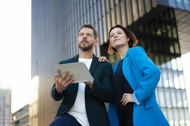 Geschäftsfrau mit Hand auf der Hüfte, die mit einem Kollegen steht, der einen Tablet-PC hält - MOEF04406