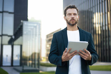 Contemplative businessman holding tablet PC in front of building - MOEF04414