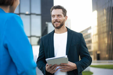 Businessman holding tablet PC talking to colleague - MOEF04421