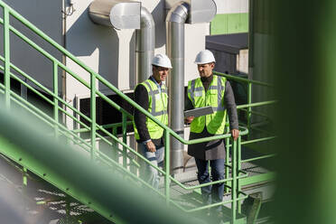 Ingenieure mit Schutzhelmen diskutieren an einem sonnigen Tag in einer Recyclinganlage - DIGF19149