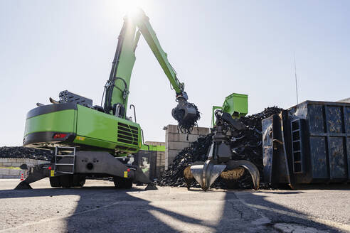 Bagger hebt an einem sonnigen Tag Gummireifen in einer Recyclinganlage - DIGF19209