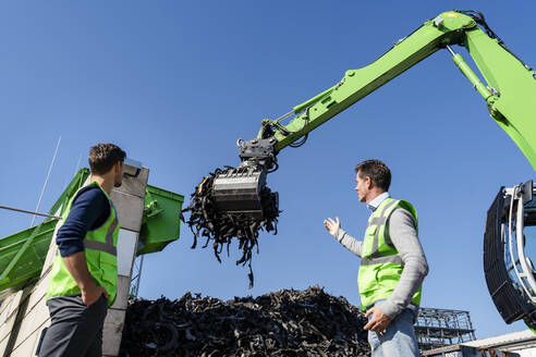 Älterer Mann diskutiert mit einem Kollegen über einen Bagger im Recyclingzentrum - DIGF19232