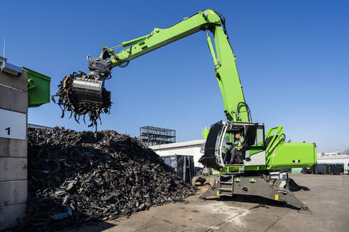 Mature man operating excavator and lifting rubber waste at recycling center - DIGF19237