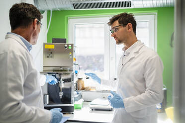 Mature scientist discussing over machine with colleague at laboratory - DIGF19259