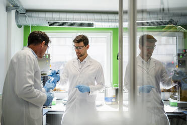 Mature scientist with colleague discussing over thermolysis experiment at laboratory - DIGF19261