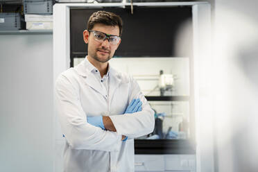 Smiling scientist in lab coat standing with arms crossed at laboratory - DIGF19277