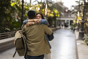 Happy woman embracing man on footpath in park - JCCMF07771