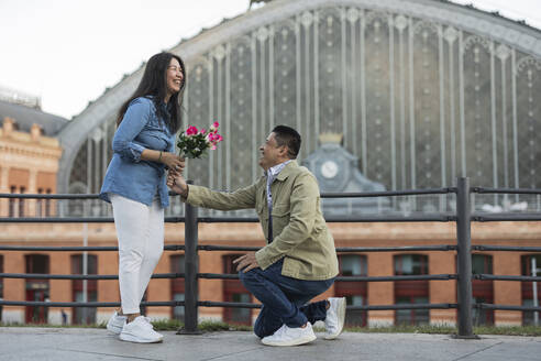 Glücklicher Mann, der einer Frau Blumen schenkt und ihr am Valentinstag auf dem Fußweg einen Antrag macht - JCCMF07791