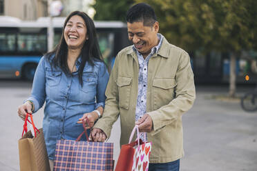 Glücklicher Mann und Frau mit Einkaufstüten auf dem Fußweg - JCCMF07793