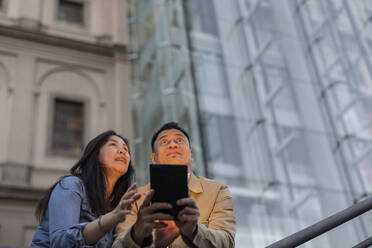 Man holding tablet PC standing by woman in front of building - JCCMF07802