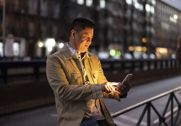 Mature man using smart phone sitting on railing - JCCMF07811