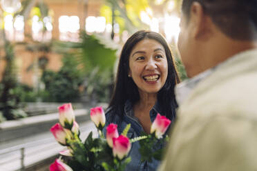 Happy mature woman with flowers looking at boyfriend on Valentine's Day - JCCMF07832