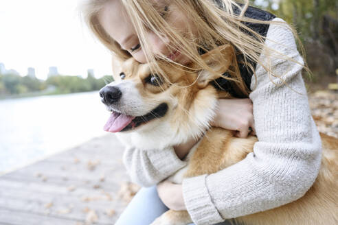 Smiling blond woman embracing Pembroke welsh Corgi - EYAF02303