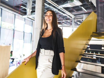 Lächelnde Geschäftsfrau beim Abstieg von der Treppe im Büro - AMRF00139