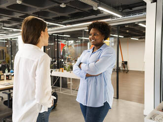 Businesswoman with arms crossed talking with colleague in office - AMRF00142