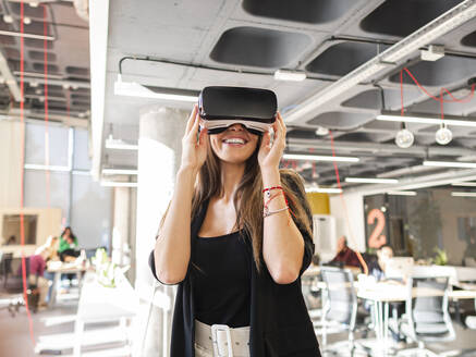 Lächelnde Geschäftsfrau mit futuristischer Brille im Büro stehend - AMRF00146