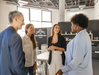 Happy businessman talking with businesswomen in cafeteria - AMRF00148