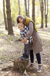 Happy boy standing on tree stump with mother in park - ONAF00199