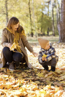 Glückliche Mutter und Sohn in hockender Position mit gelbem Blatt im Park - ONAF00204