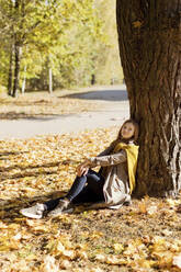 Frau lehnt an einem Baum im Park an einem sonnigen Tag - ONAF00206