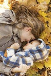 Frau liegt mit Sohn auf gelben Herbstblättern im Park - ONAF00216