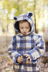 Niedlicher Junge mit Kapuzenjacke, der ein Blatt im Park hält - ONAF00228