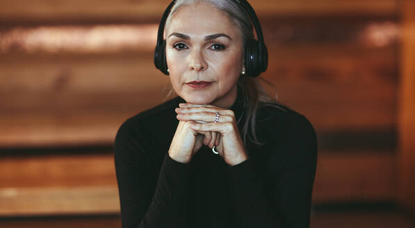 Closeup portrait of senior woman listening music on headphones. Beautiful mature woman listening to music in headphones at cafe. - JLPSF23904
