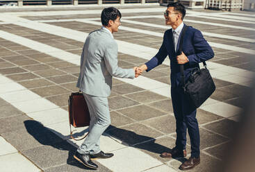 Two asian businessmen shaking hands outdoors in the city. Business people greeting each other outdoors. - JLPSF23913